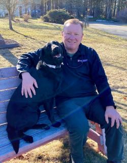 Scott Smith sitting on a bench with his black Labrador Retriever named Judy