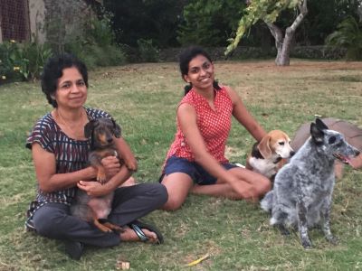 Dr. Sree Rajeev and her daughter Dr. Malavika Rajeev sitting in the grass with their 3 dogs